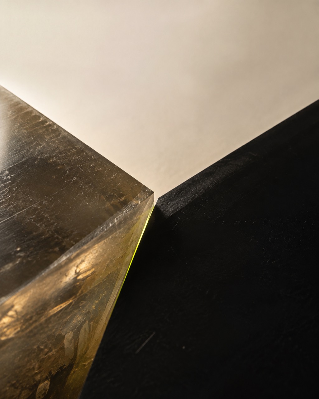 A translucent warm bone resin mass pressed against a dense matte-black slab, with a narrow seam under visible tension.